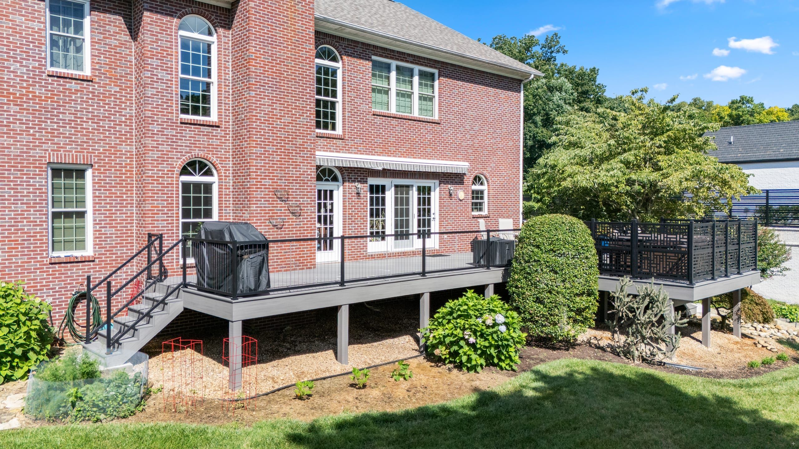 Rear view of the Wilshire elevated composite deck from the yard, with black cable railing and stairs to grade