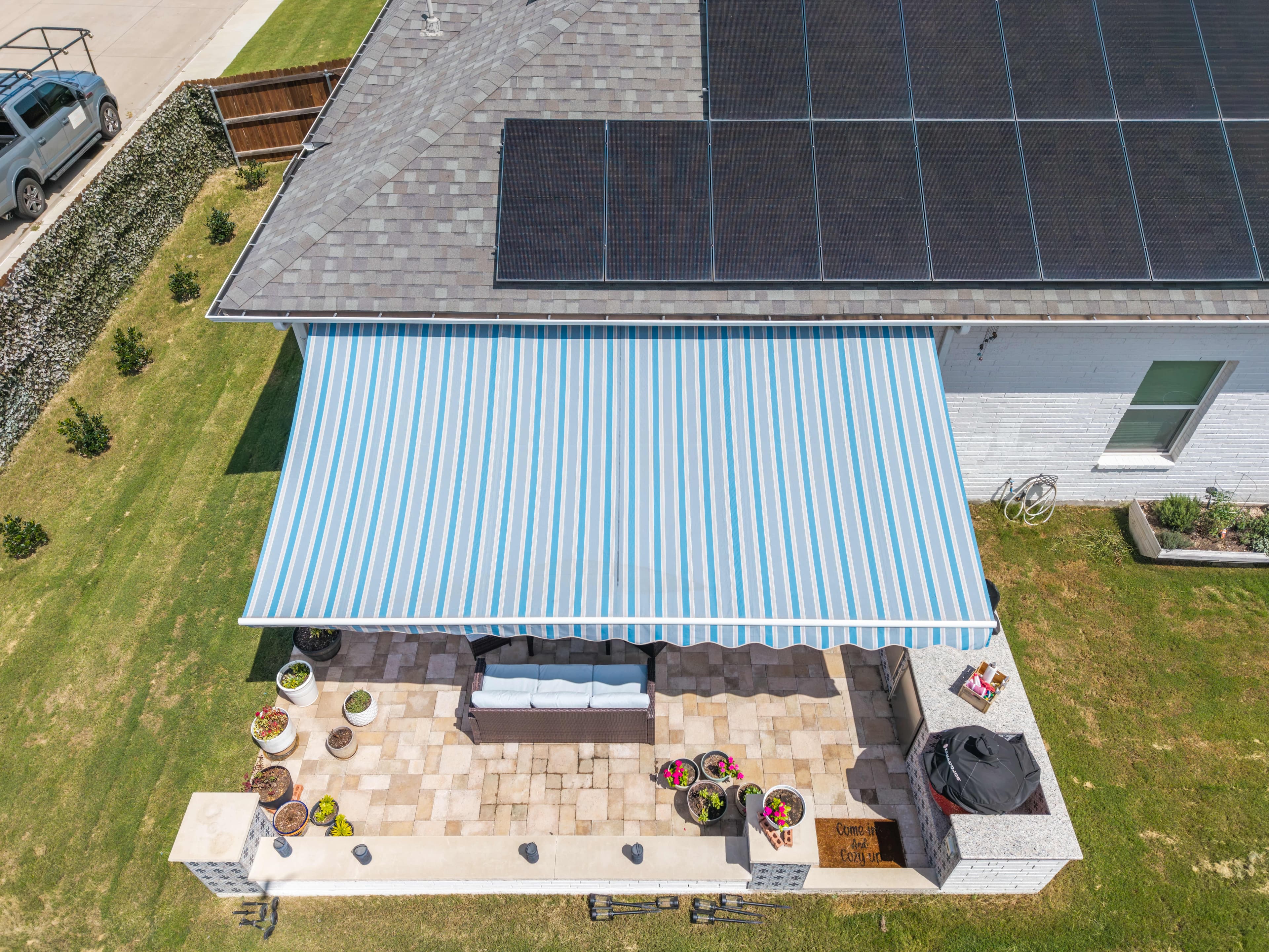 Aerial view of a blue-striped retractable awning shading a patio outdoor kitchen