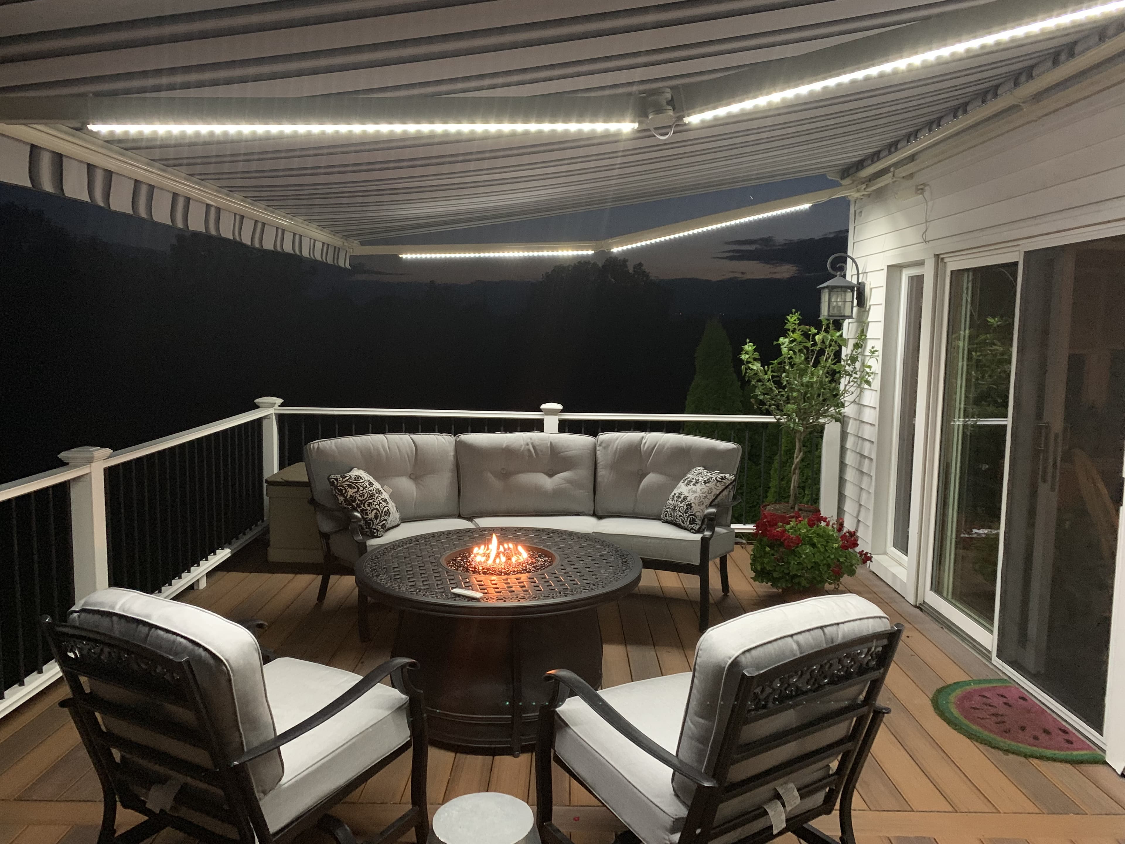 Retractable awning with LED lighting over a nighttime deck with fire pit and patio seating